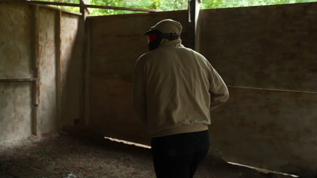 Handheld footage following a paintball player through a wooden course.