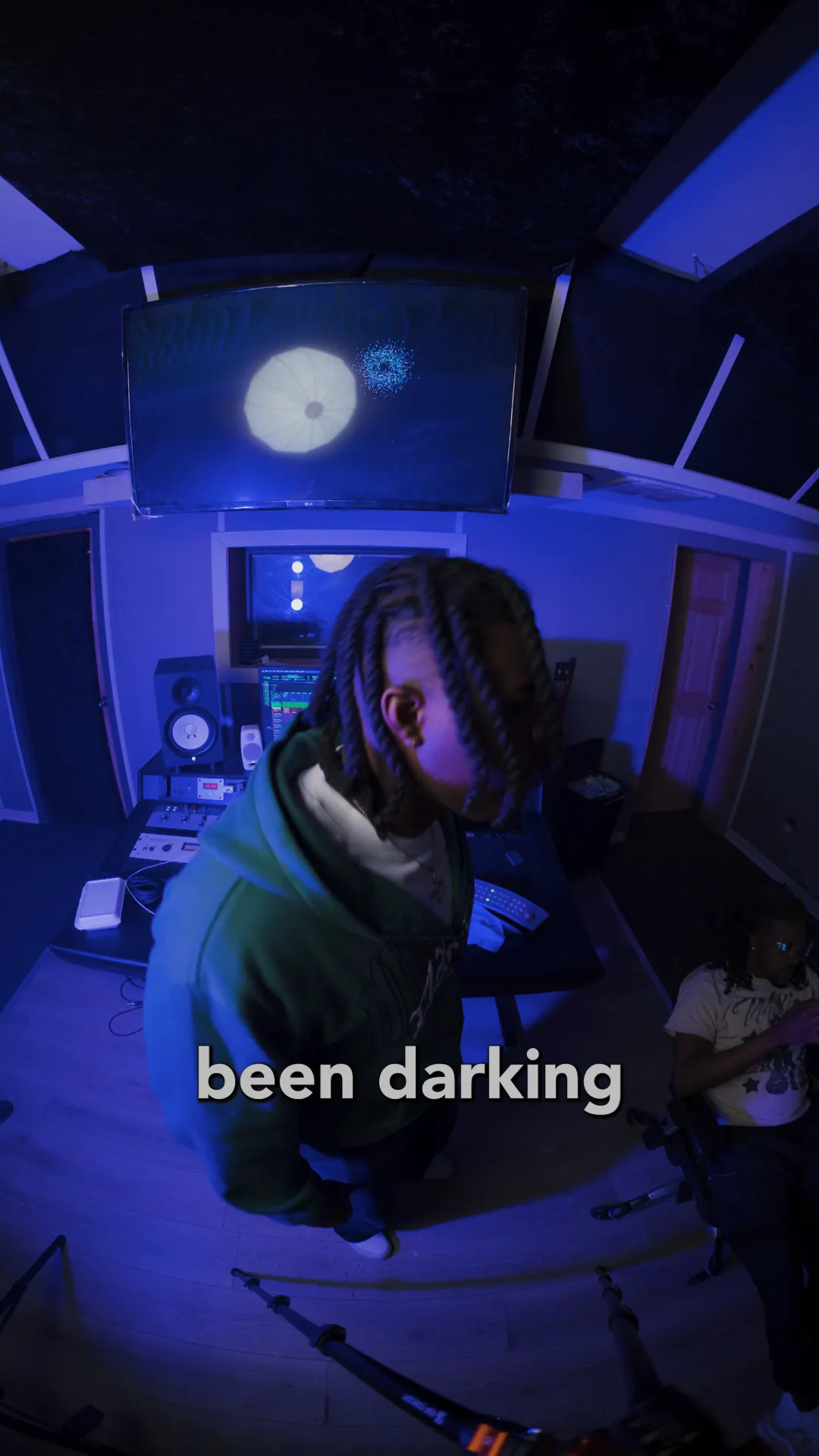 Fisheye performance video: an artist raps in a purple-lit studio, lyrics on screen.